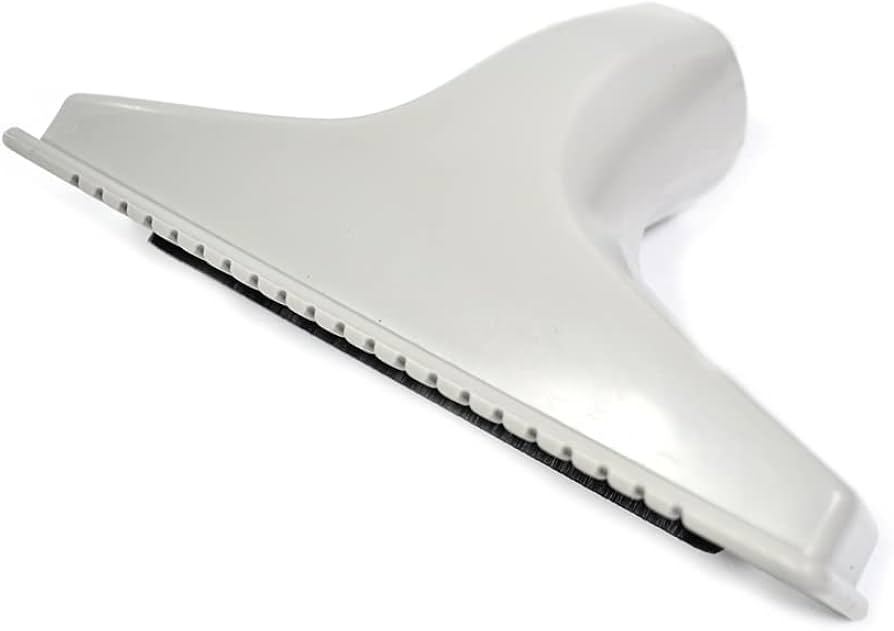 A real photo close-up of a hand using a vacuum crevice attachment along the seam of a button-tufted fabric sofa, with the button and stitching clearly visible