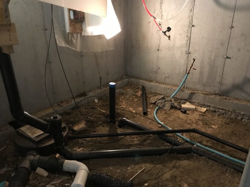 A real photo of a bathroom wall with exposed drain and water supply lines during a renovation, showing the rough-in plumbing locations