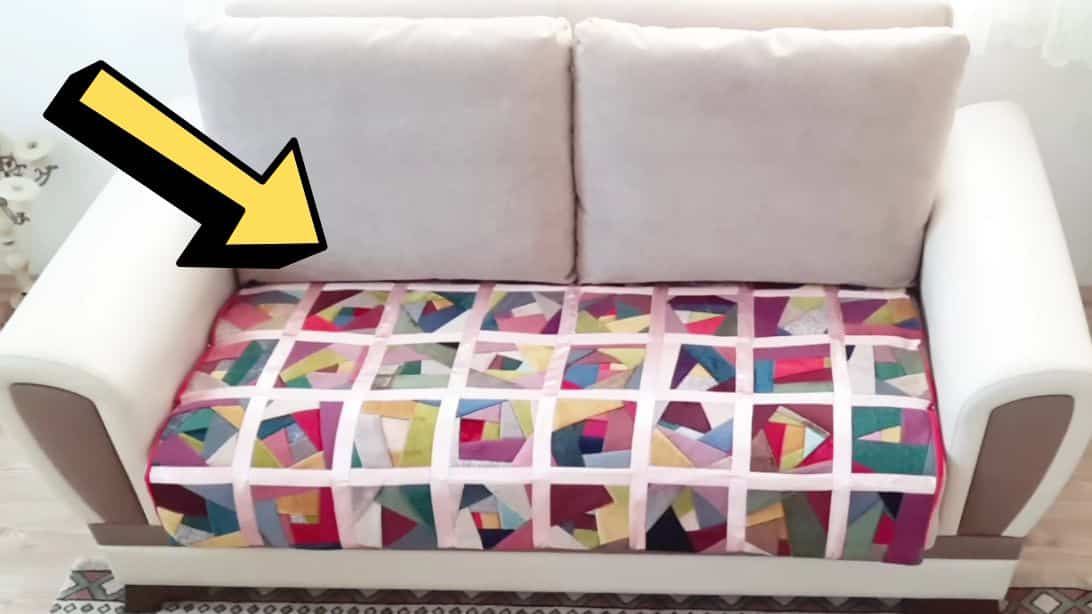 A real photo of a cozy living room sofa with a washable throw blanket spread over one seat as a craft protector, with a small container of slime on a coffee table