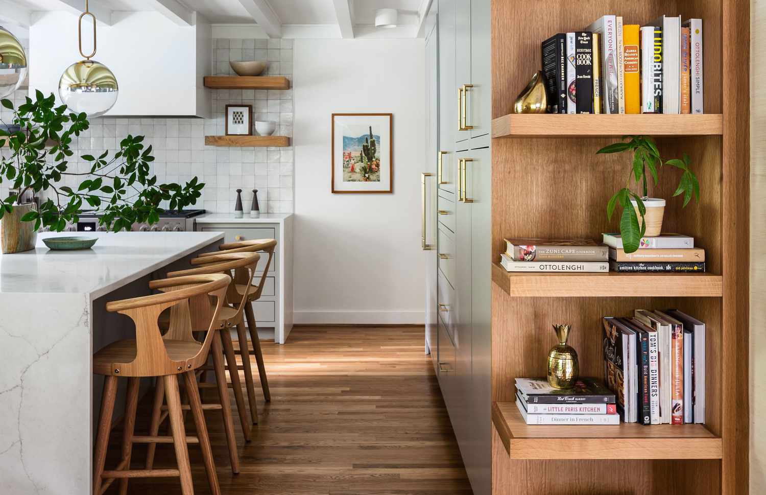 A real photo of a cozy living room wall with floating shelves styled with vintage brass frames, a small amber glass lamp, a stack of books, and a ceramic bowl, warm evening lighting