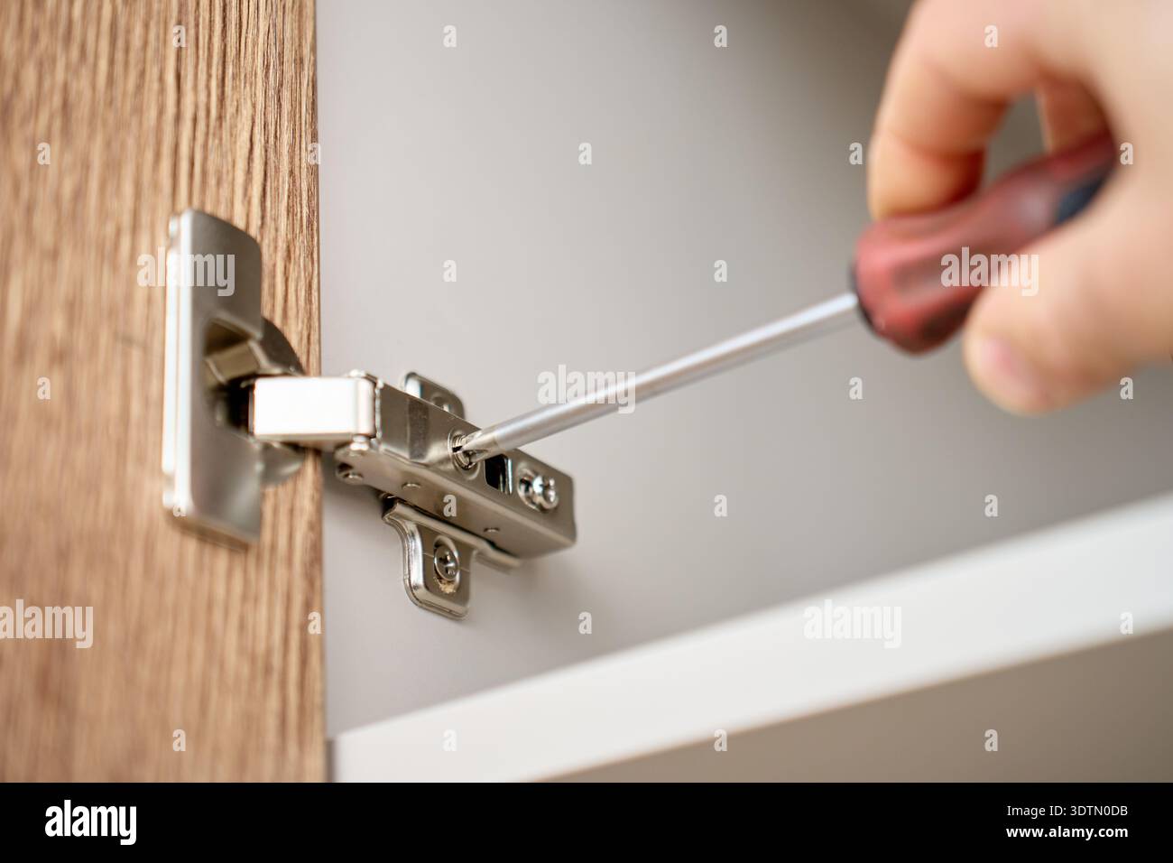 A real photo of a hand using a screwdriver to tighten brass-colored hinge screws on a white interior door