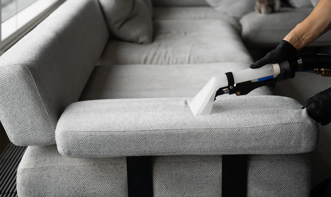 A real photo of a neutral linen-blend sofa in a bright living room, with a hand gently blotting a small spill on a cushion using a clean white cloth