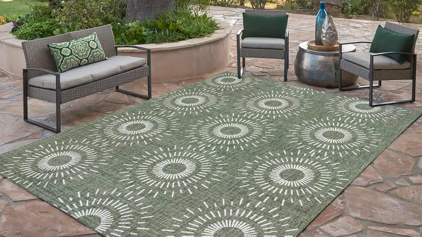 A real photo of a patterned area rug laid flat on a sunny outdoor patio with a soft brush, a bucket, white towels, and a vacuum nearby, natural light, cozy home cleaning moment