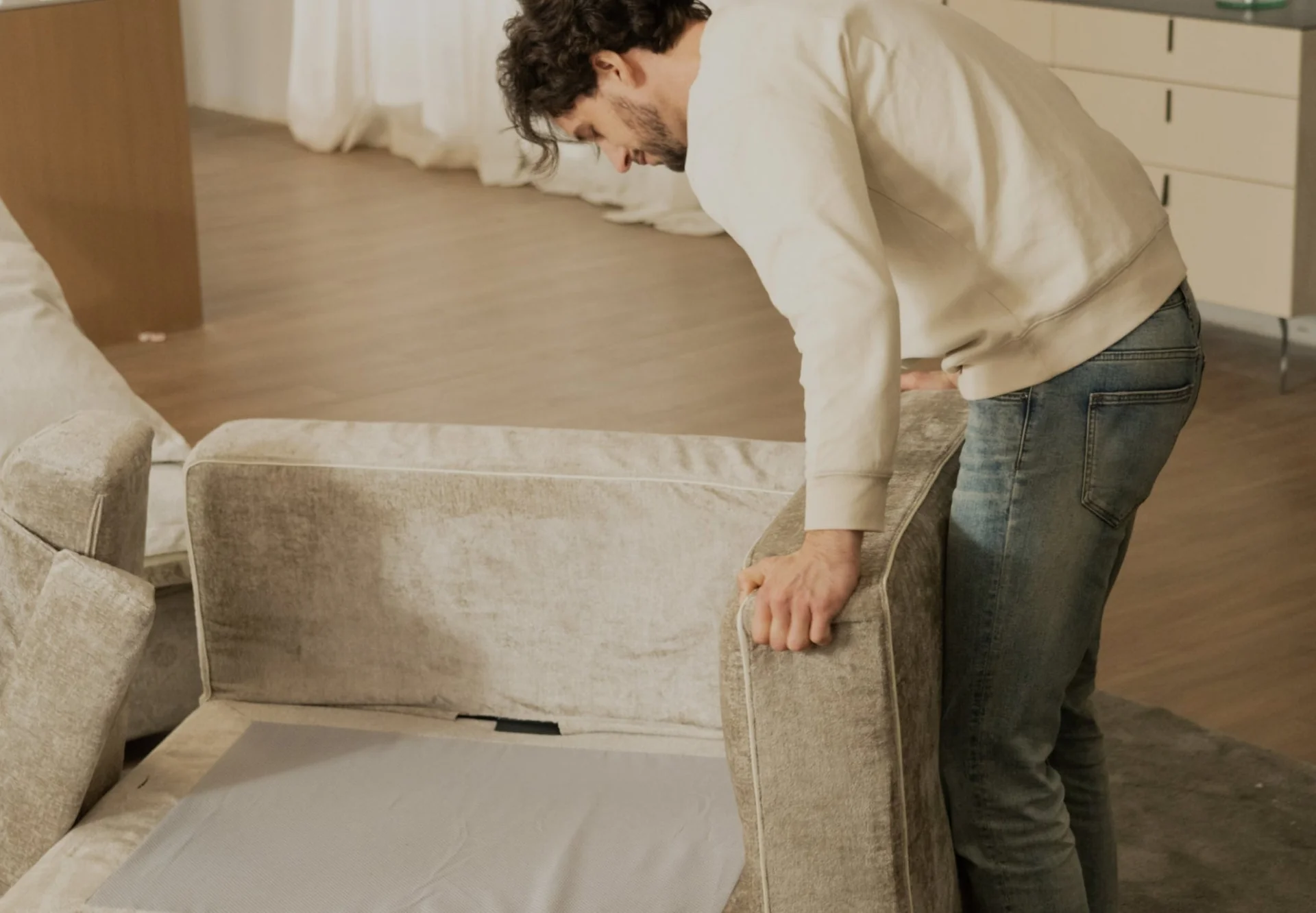 A real photo of a person scanning a fabric couch cushion seam with a small UV flashlight in a dim room, focusing on the piping and corner where stains can hide
