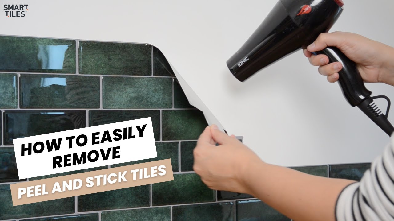 A real photo of a person using a hair dryer to gently warm and peel off a peel-and-stick backsplash tile from a kitchen wall, with slow removal to protect the paint