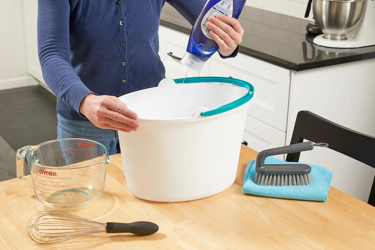 A real photo of basic upholstery cleaning supplies including baking soda, white vinegar, microfiber cloths, and a spray bottle arranged on a kitchen counter