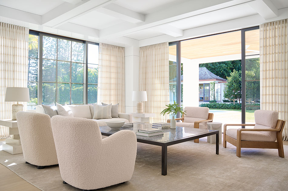 A real photo of beige linen curtain panels stacked neatly on the left side of a sliding glass door, showing most of the glass uncovered with sunlight streaming onto a wood floor