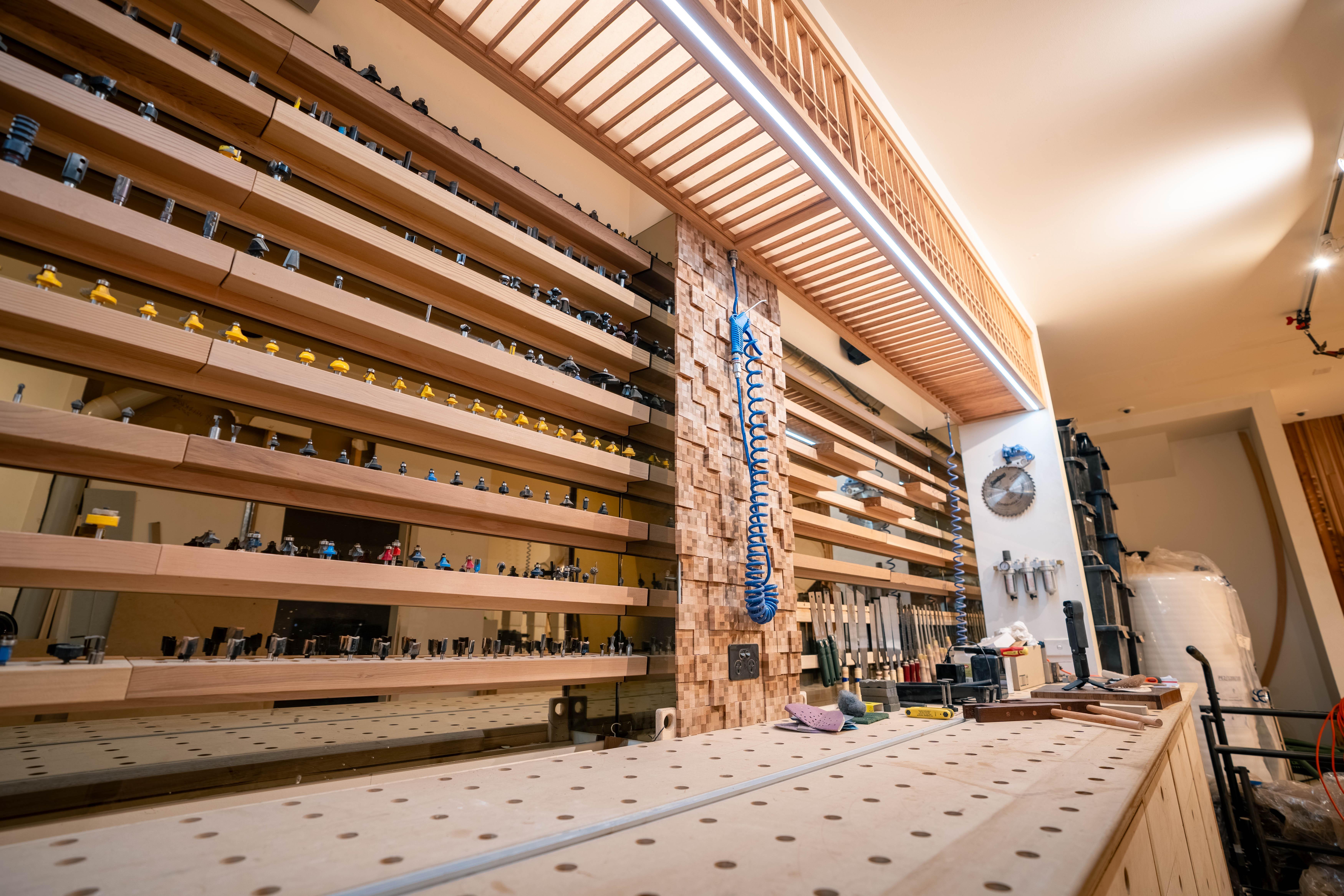A real photo of hands holding a wooden French cleat against the back of a large framed mirror, with a drill and screws on a workbench