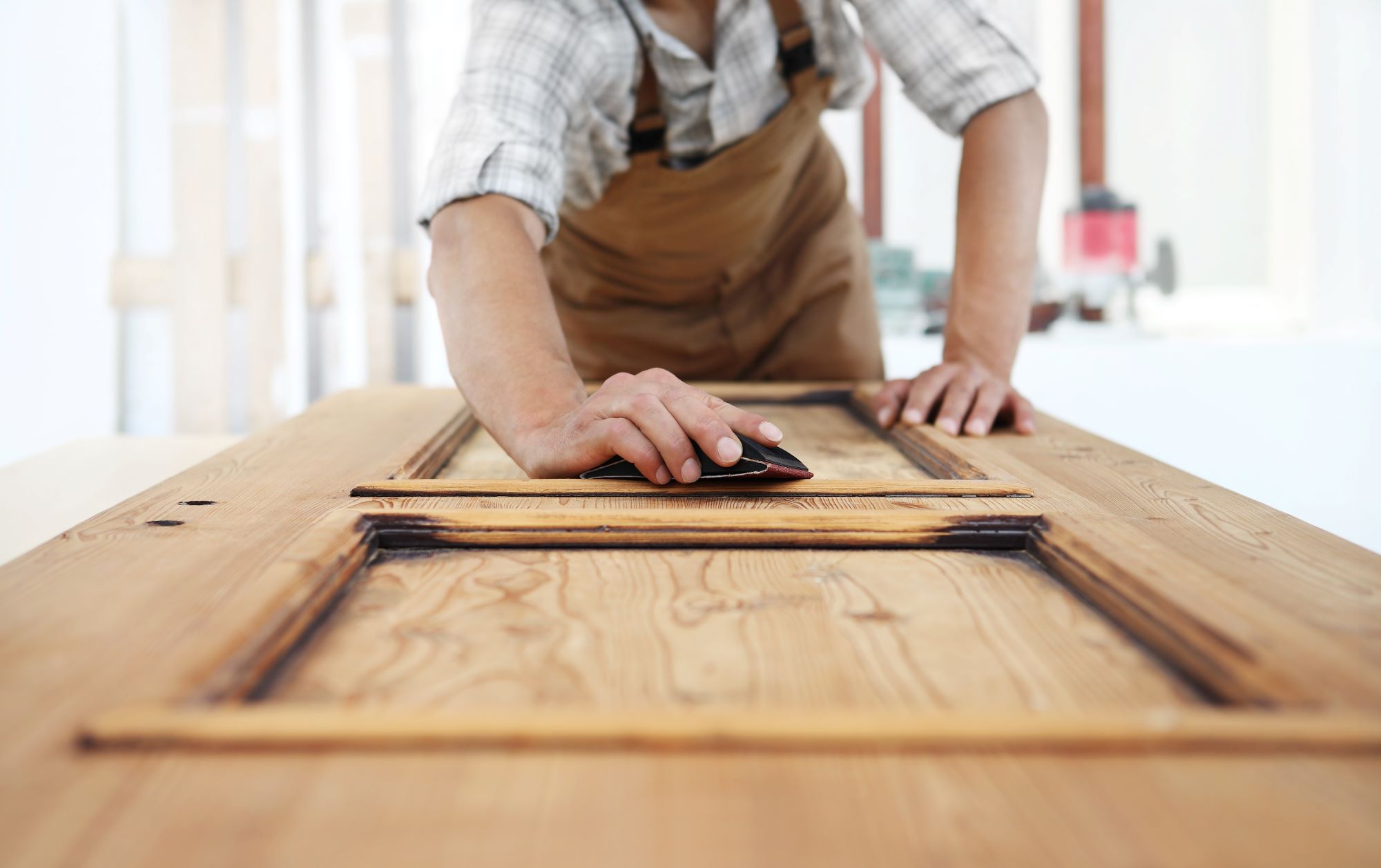 A real photo of hands sanding the edge of a white interior door with sandpaper, with the door laid flat on sawhorses