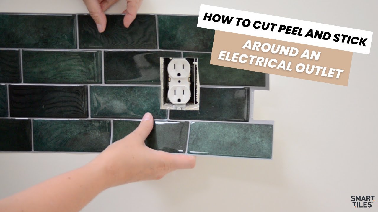 A real photo of hands using a utility knife and metal ruler to cut a peel-and-stick tile sheet to fit around a standard kitchen electrical outlet opening