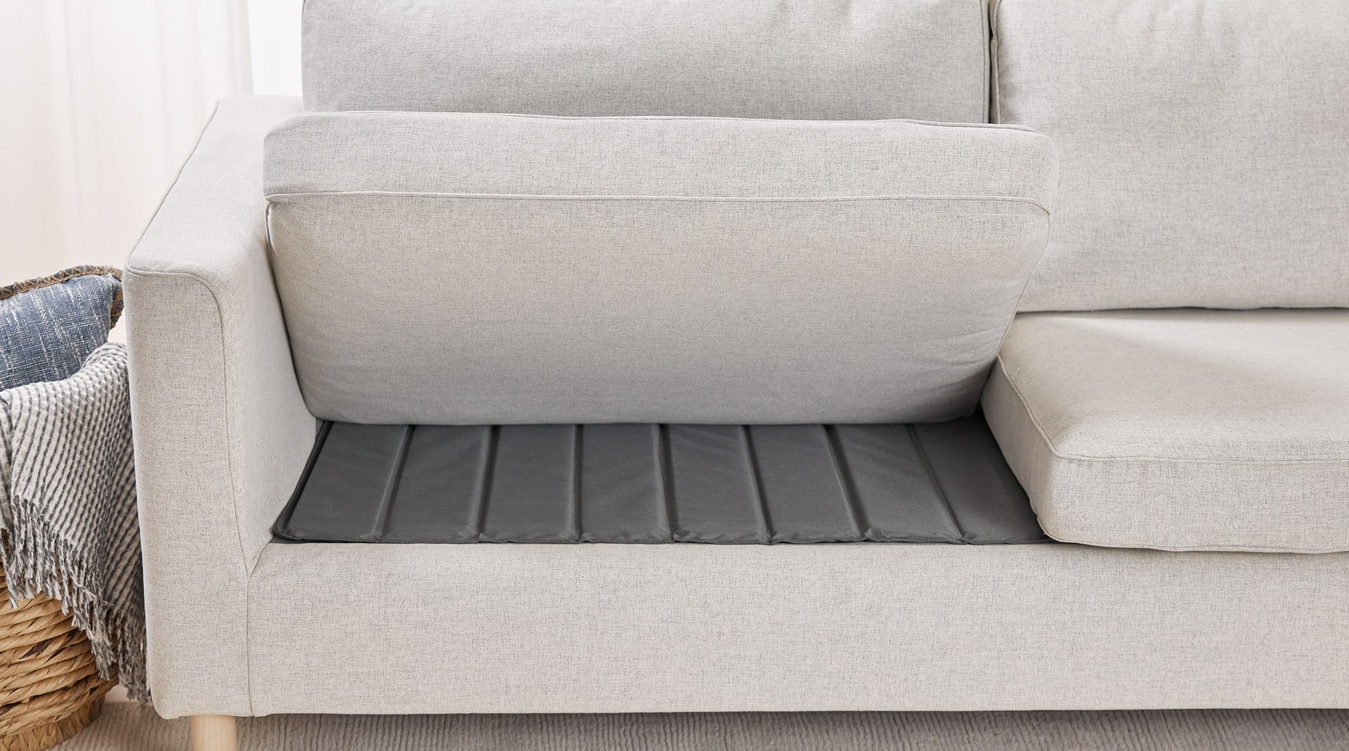 A real photograph of a couch with the seat cushions removed, showing a neatly cut plywood panel placed on the seat deck as extra support