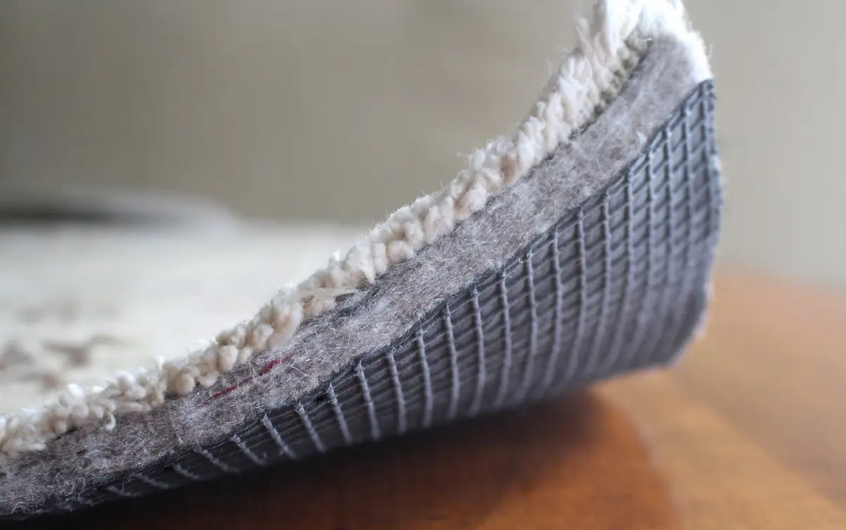 A real photograph of a felt-and-rubber combo rug pad folded to show layers on a clean hardwood floor