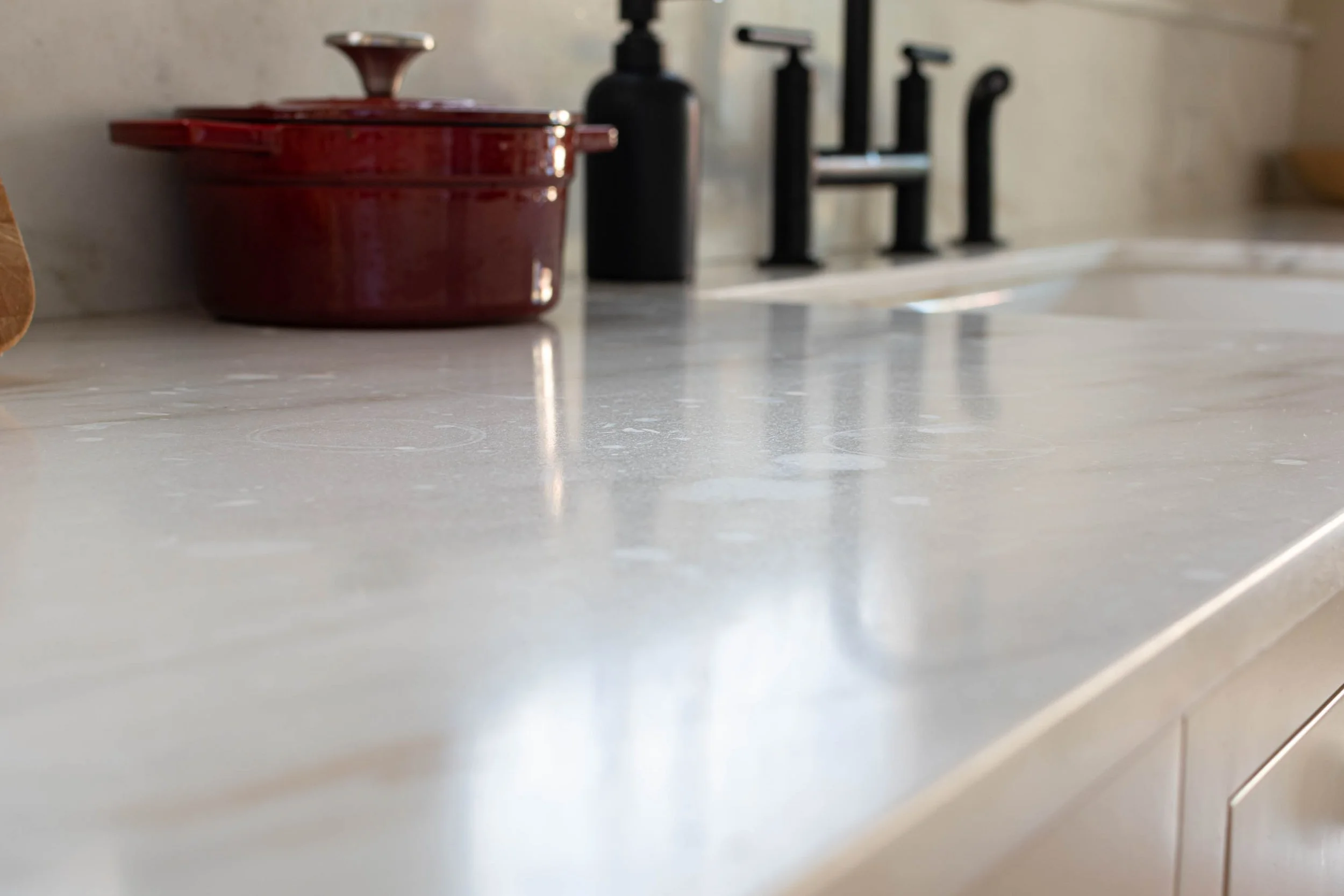 A real photograph of a marble countertop with a faint dull etched ring visible under angled raking light near a window
