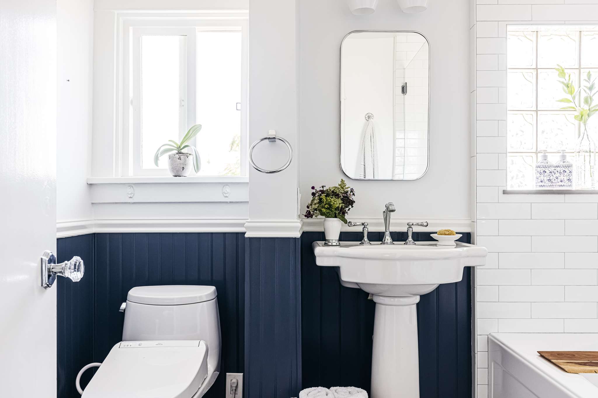 A real photograph of a small bathroom with white beadboard wainscoting, a vintage pedestal sink, and warm brass fixtures