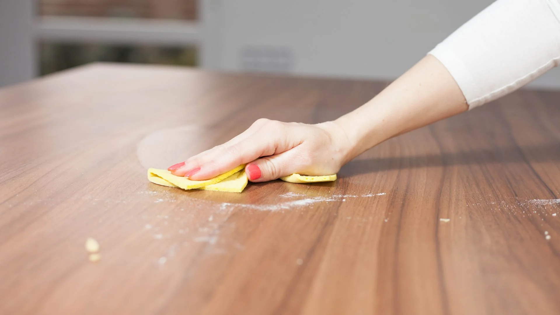A real photograph of a soft cotton cloth wiping a small area on a wooden tabletop, showing gentle cleaning in warm indoor light
