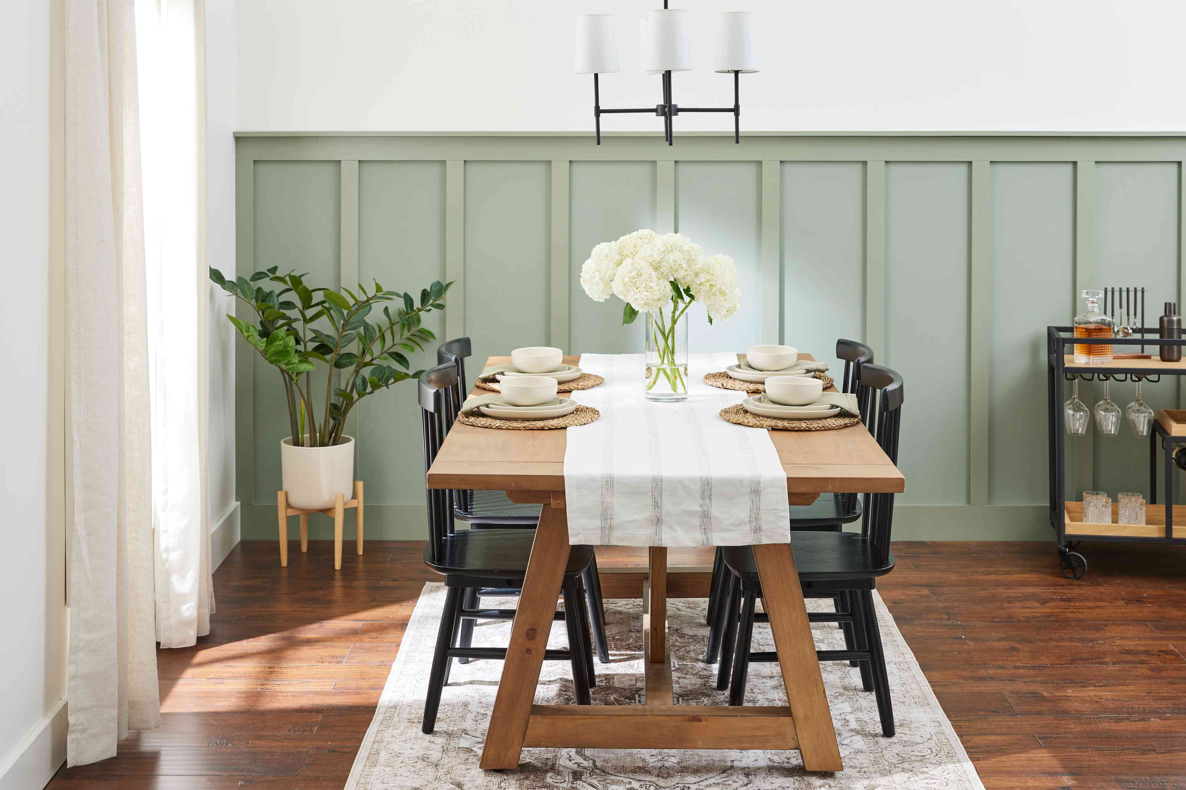 A real photograph of a traditional dining room with board and batten wainscoting painted a muted greige, a vintage wood table, and a warm pendant light