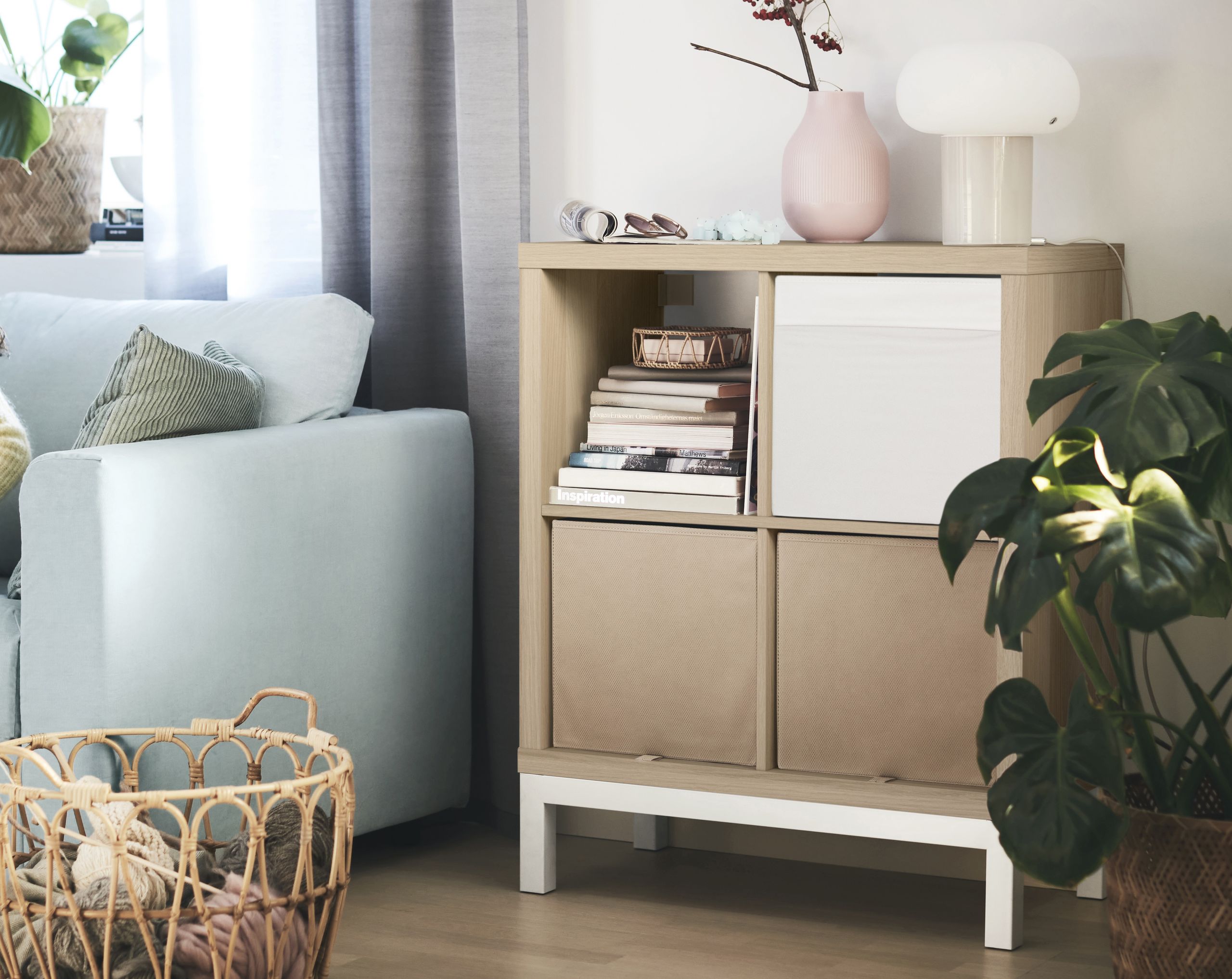 A real photograph of a white IKEA Kallax turned horizontally with tapered wood legs, styled like a low credenza in a cozy living room