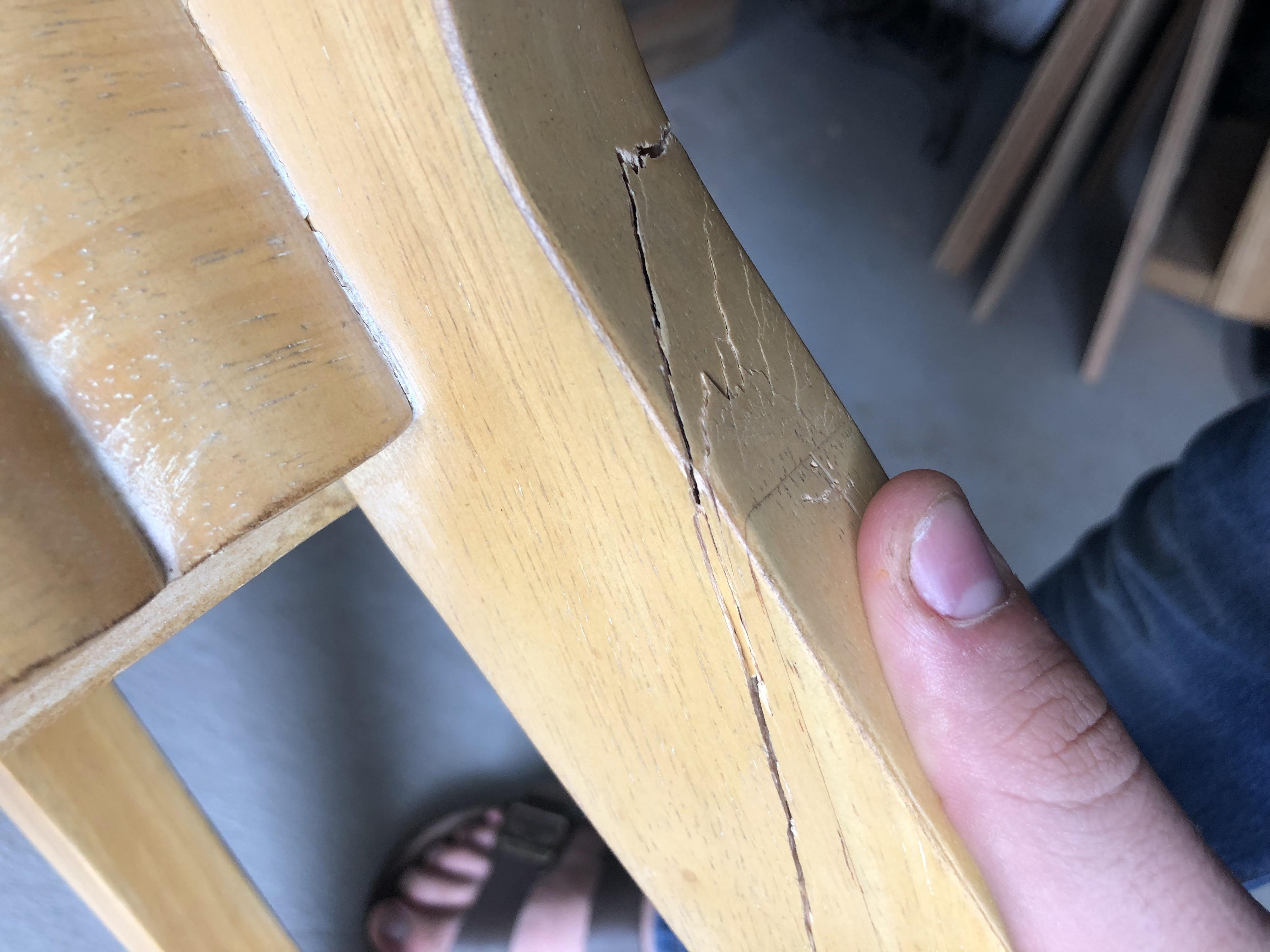 A real photograph of a wooden dining chair upside down with clamps holding a loosened joint while a bottle of wood glue sits nearby on a work surface