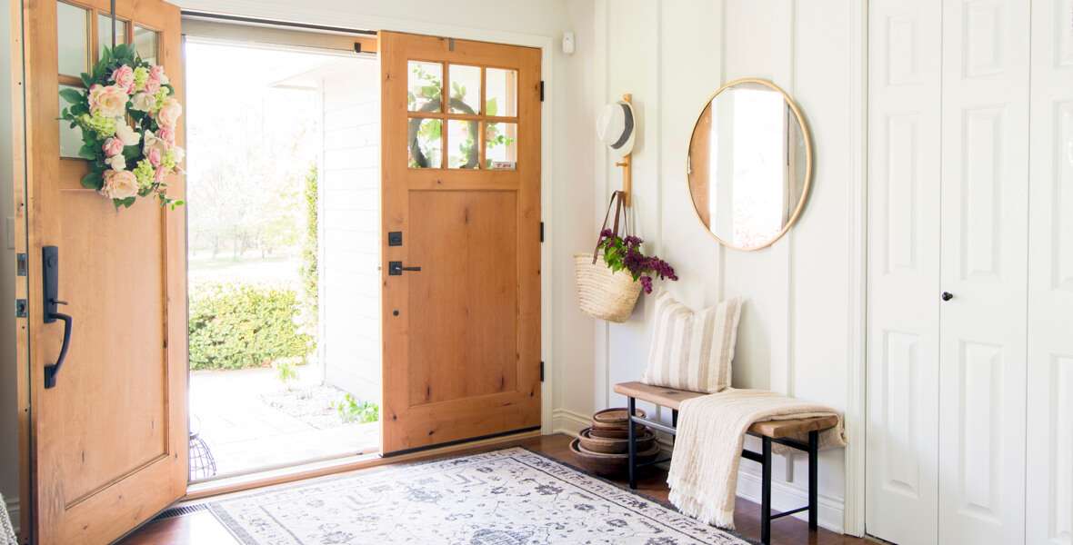 A real photograph of an entryway with tall board and batten wall molding painted a soft warm white, a simple bench, and a woven runner