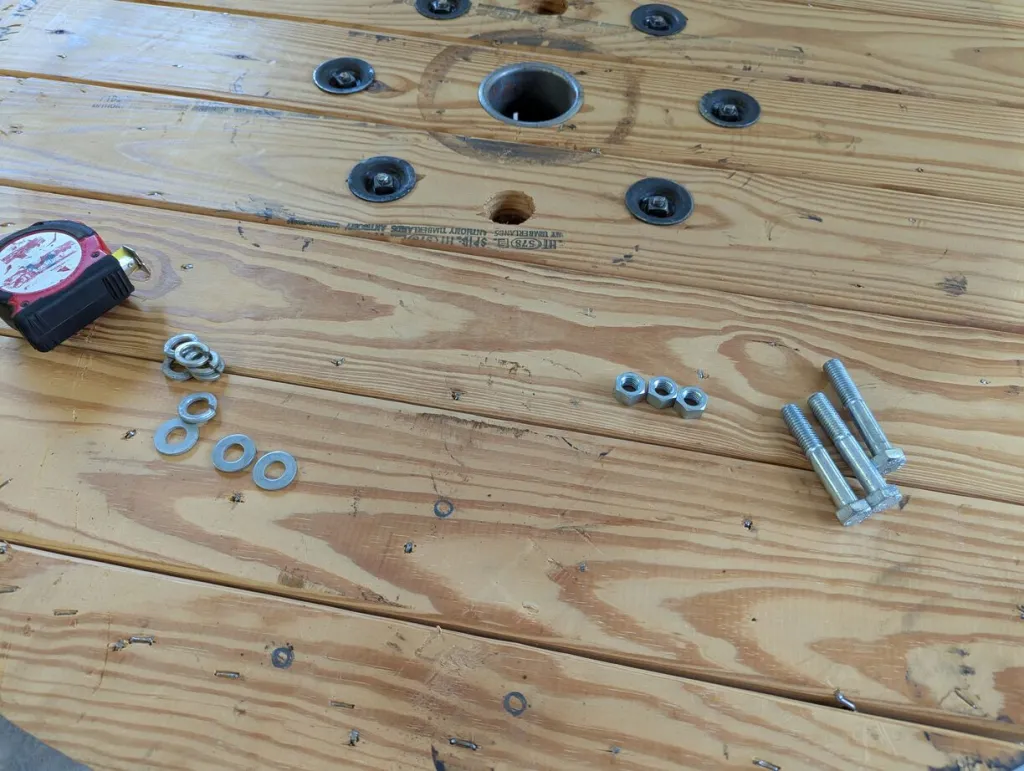 A real photograph of assorted dining chair bolts, washers, and nuts arranged on a wooden workbench next to a tape measure