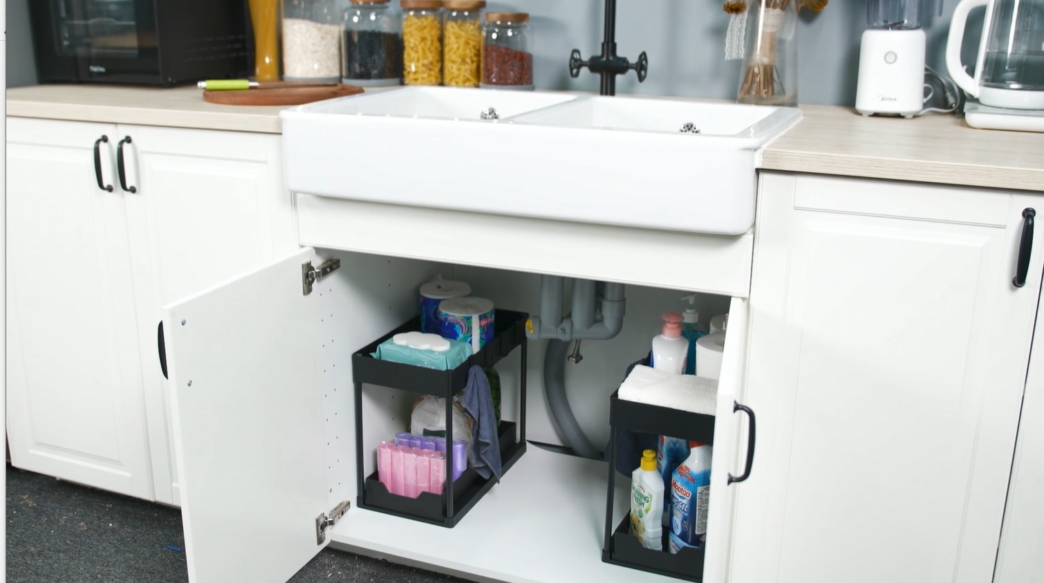 A real photograph of clear plastic storage bins and a silicone liner placed inside a bathroom under-sink cabinet with visible plumbing