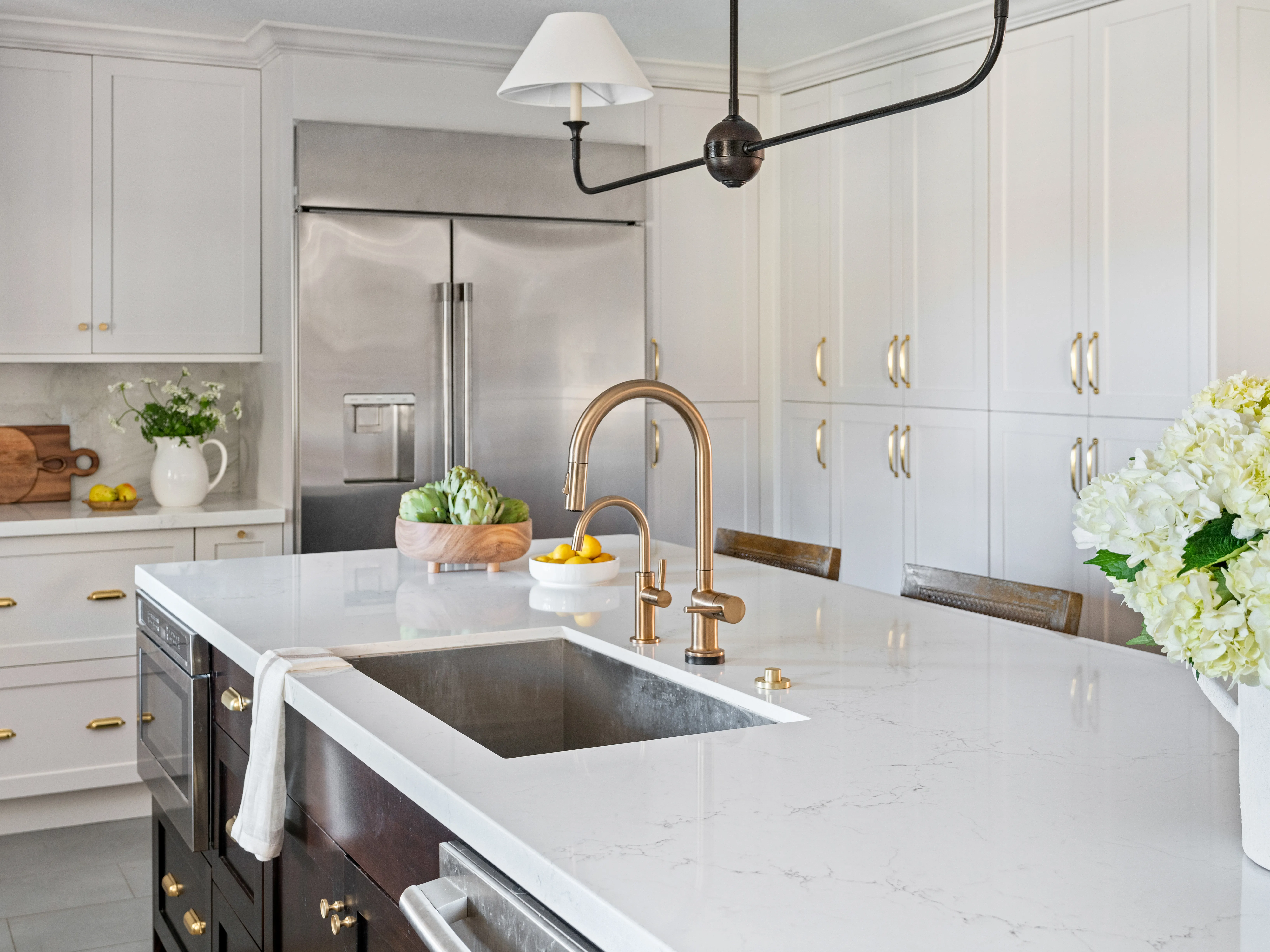 A real photograph of hands wiping down a white marble kitchen countertop with a soft microfiber cloth near a sink in warm natural morning light