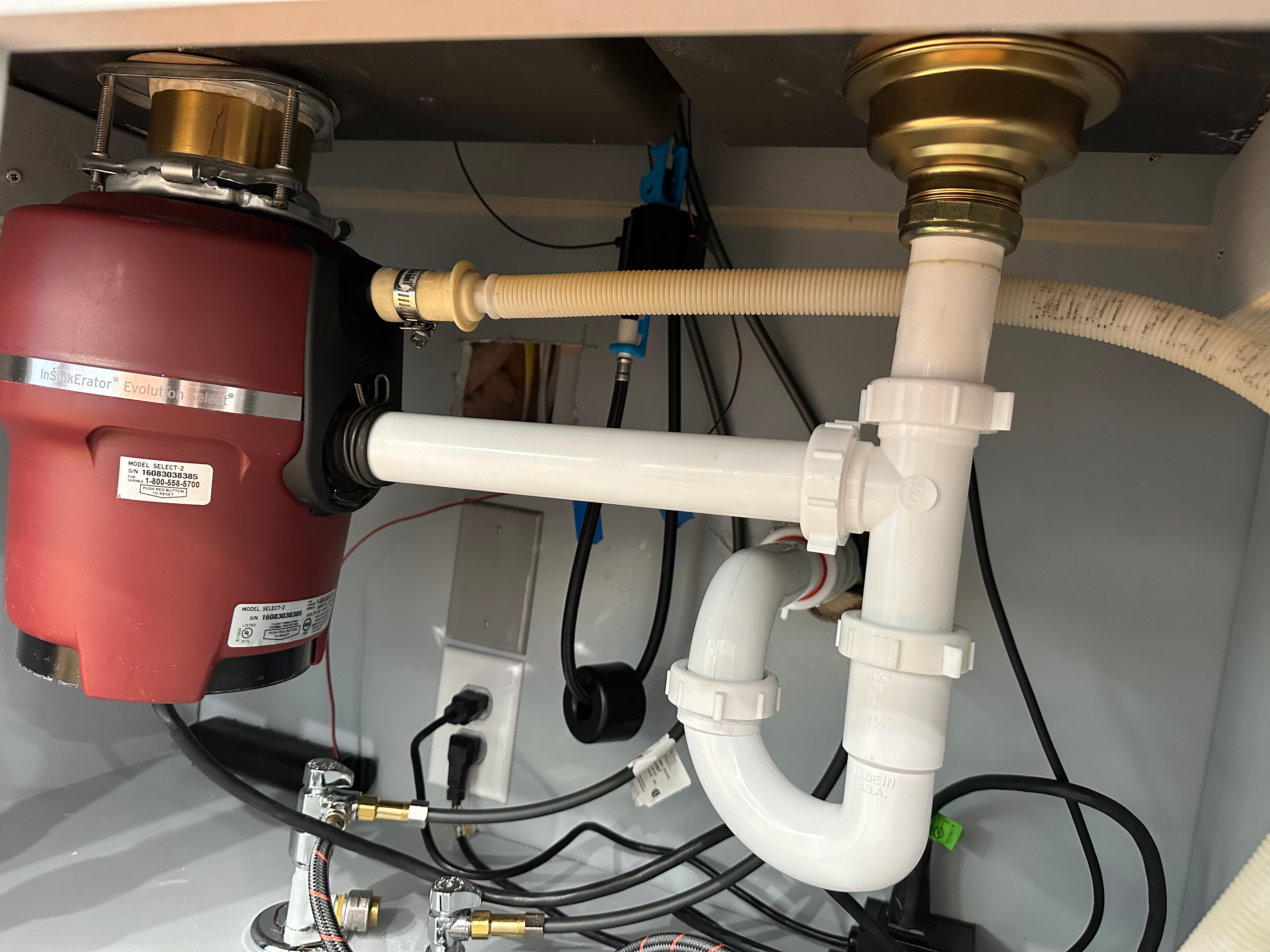 A real under-sink photo showing a garbage disposal outlet connected to a white P-trap and drain pipe, with light reflecting off the fittings