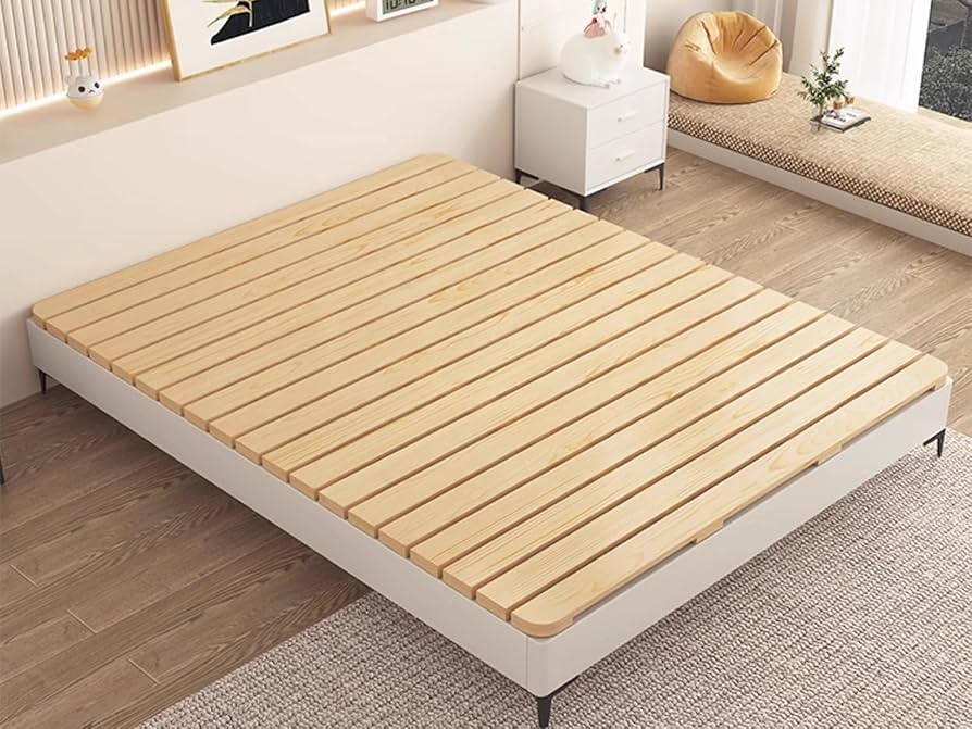 A realistic photo of a bunkie board laid neatly across wooden bed slats in a bedroom, showing even support
