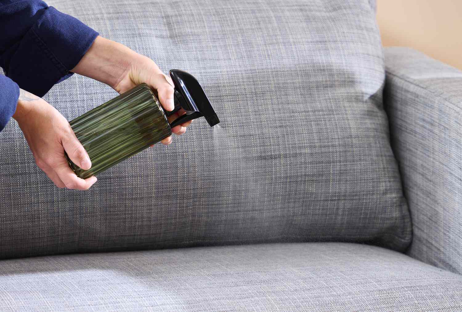 A realistic photo of a person lifting a sofa seat cushion and checking the fabric underneath in a bright living room