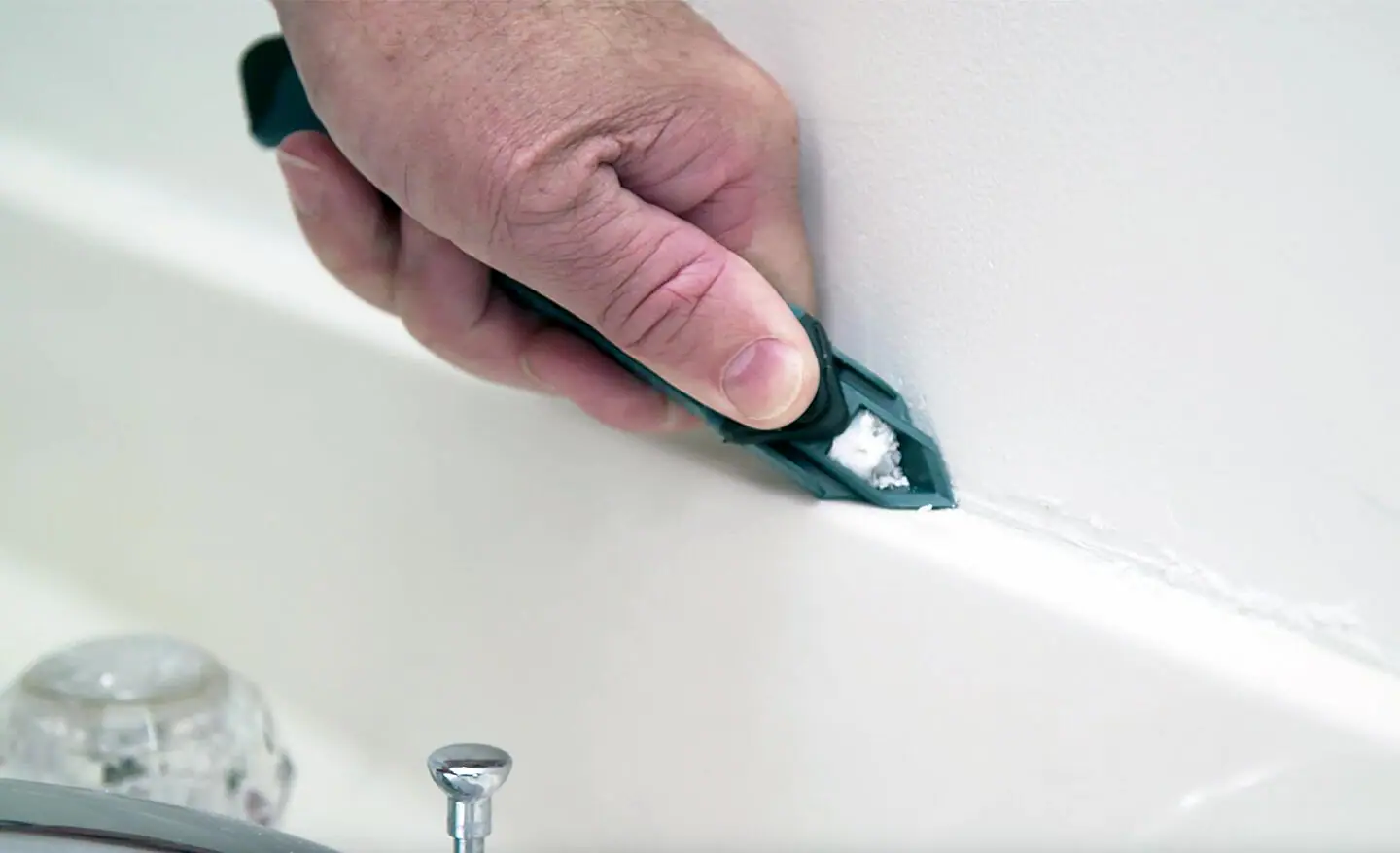 A renter on a small step stool applying a thin bead of paintable caulk along the wall to ceiling seam in a bright apartment living room, realistic home repair photograph