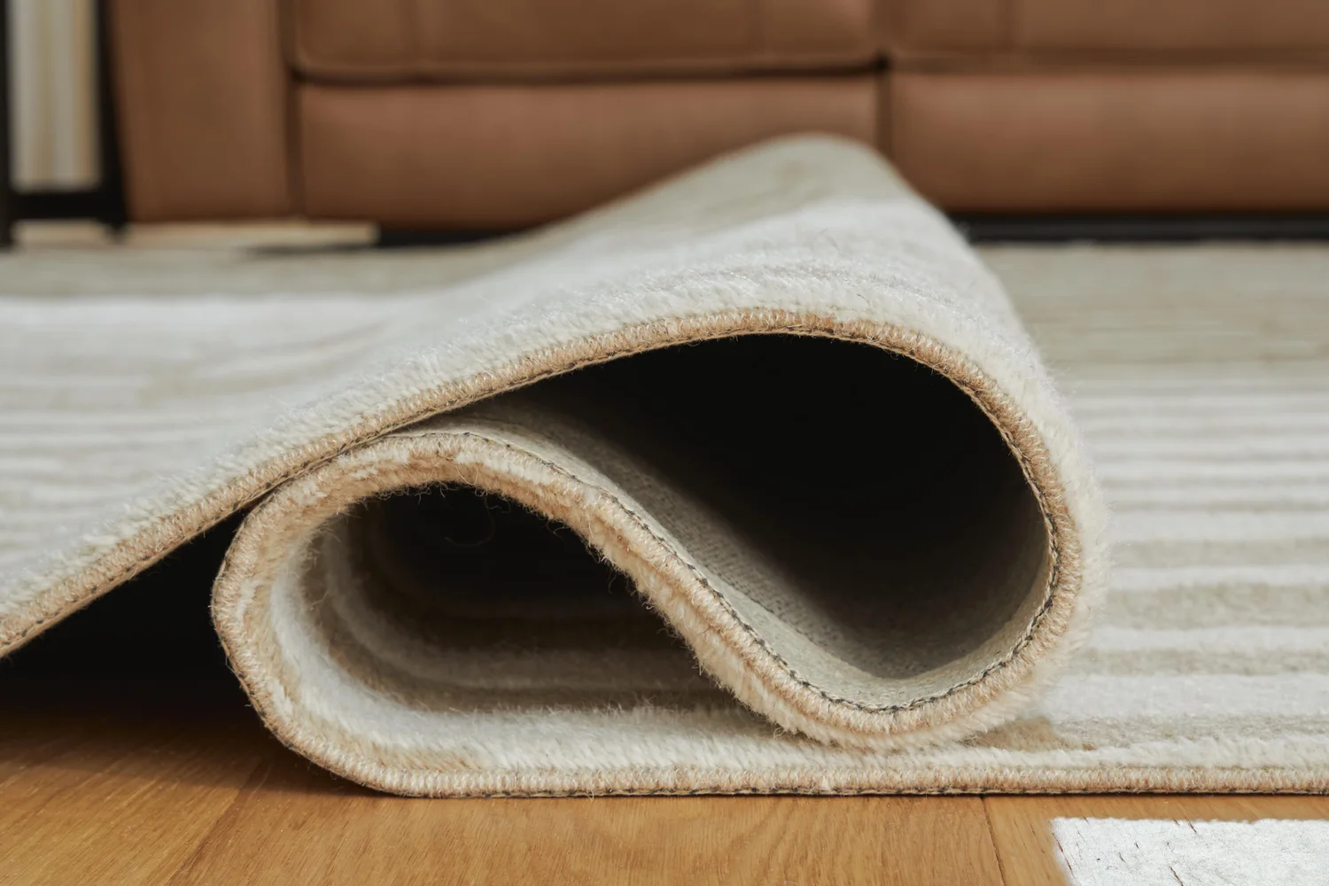 A rolled area rug leaning against a wall in a living room with bare vinyl flooring visible, suggesting the rug has been removed to help air out odors