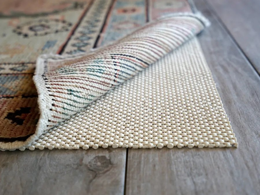 A rolled-up rug pad with a rubbery waffle texture next to a discolored rectangular area on a hardwood floor