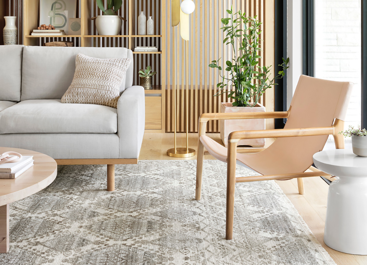 A sectional sofa with its front legs placed on a textured area rug over hardwood flooring in a warm, softly lit living room