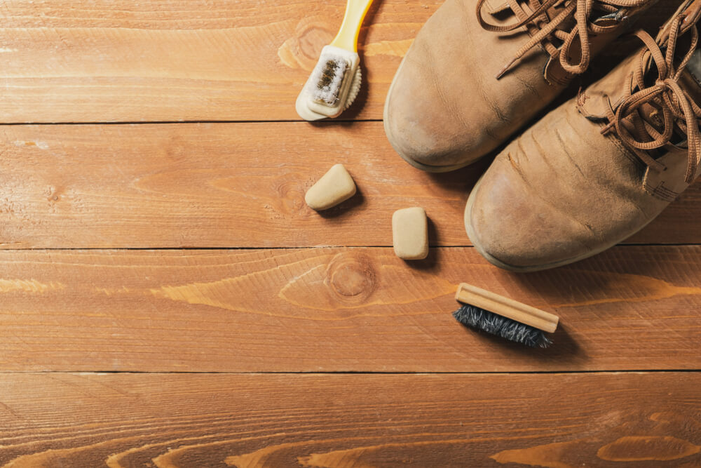 A simple suede brush and a suede eraser sitting on a wooden coffee table next to a folded white microfiber cloth