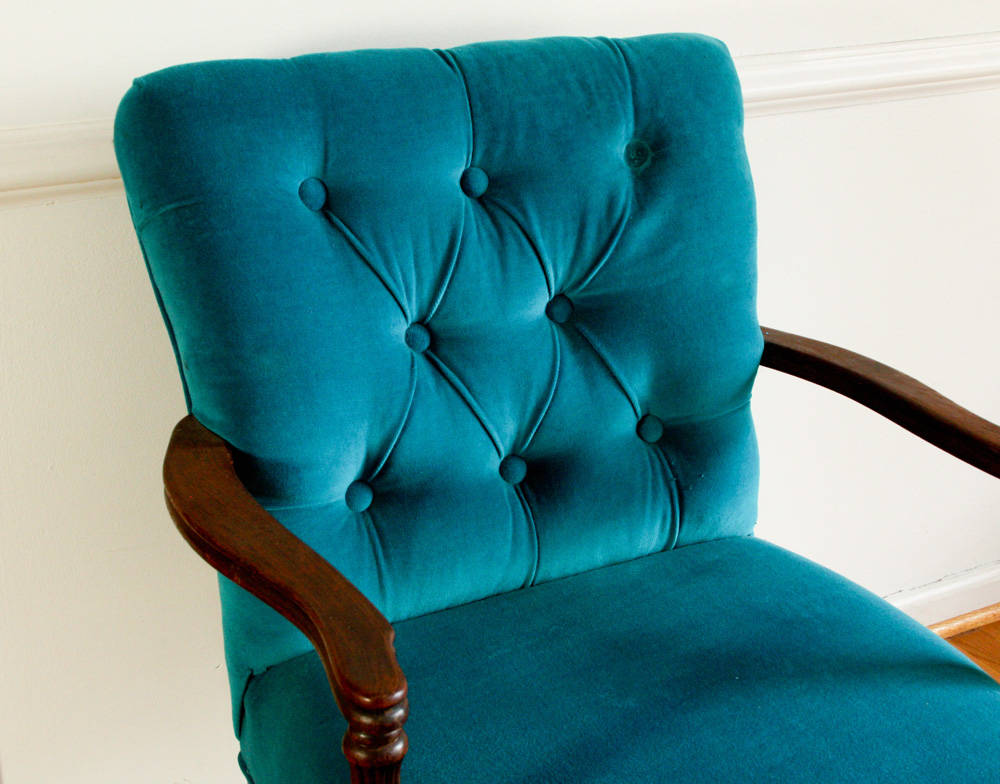 A single fabric-covered upholstery button resting on matching headboard fabric, showing the metal shank loop on the back