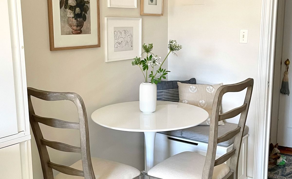 A small apartment dining nook with a round pedestal table, two chairs, a bench on the wall side, and a pendant light casting a warm glow