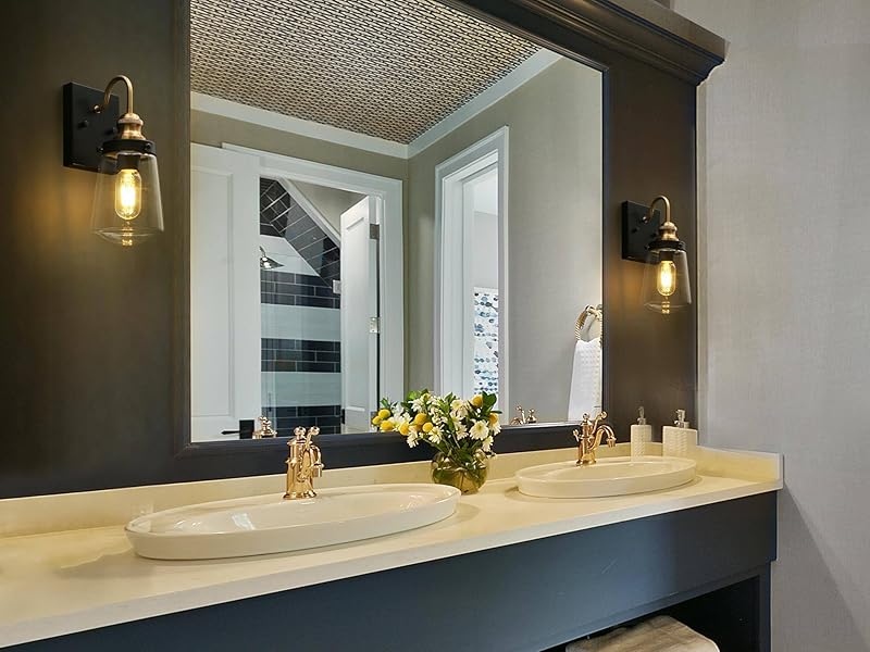 A small bathroom vanity with a thin brass-framed mirror, matte black wall sconces, and creamy off-white tile in soft evening light