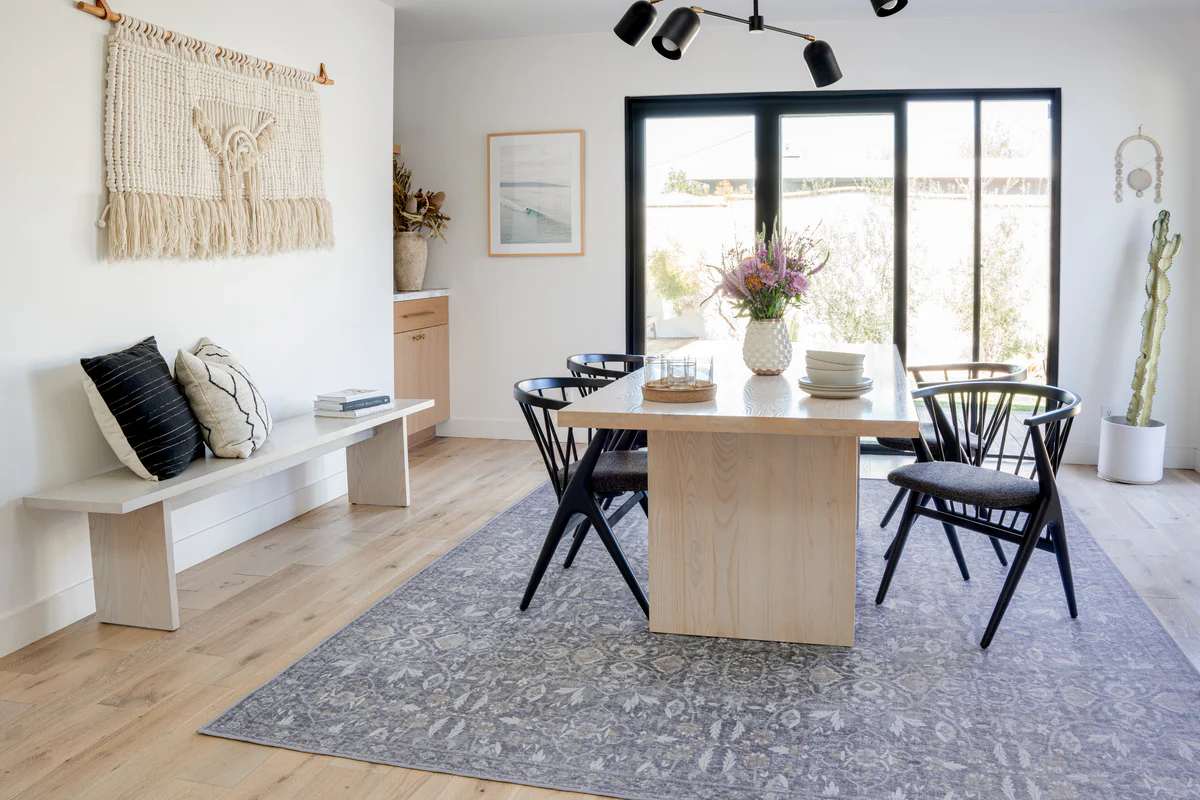 A small dining room with a patterned flatweave rug extending beyond the table, chairs pulled out smoothly with plenty of rug under the chair legs