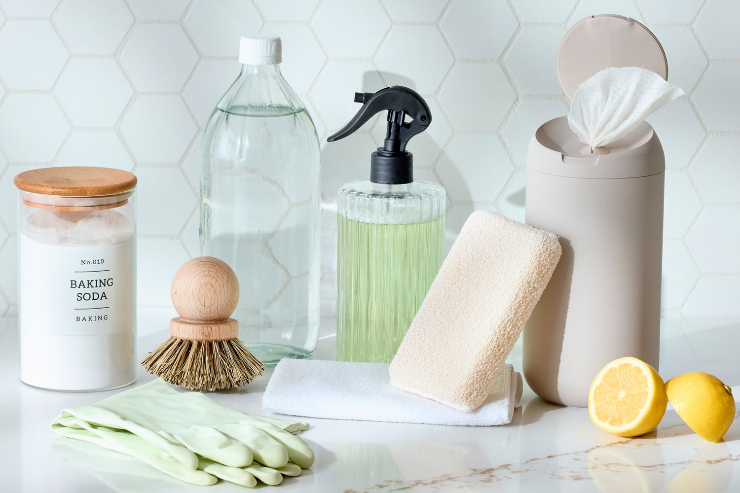 A small set of wall-cleaning supplies on a wooden table including a microfiber cloth, a small bowl, baking soda, and a melamine sponge, real home photo