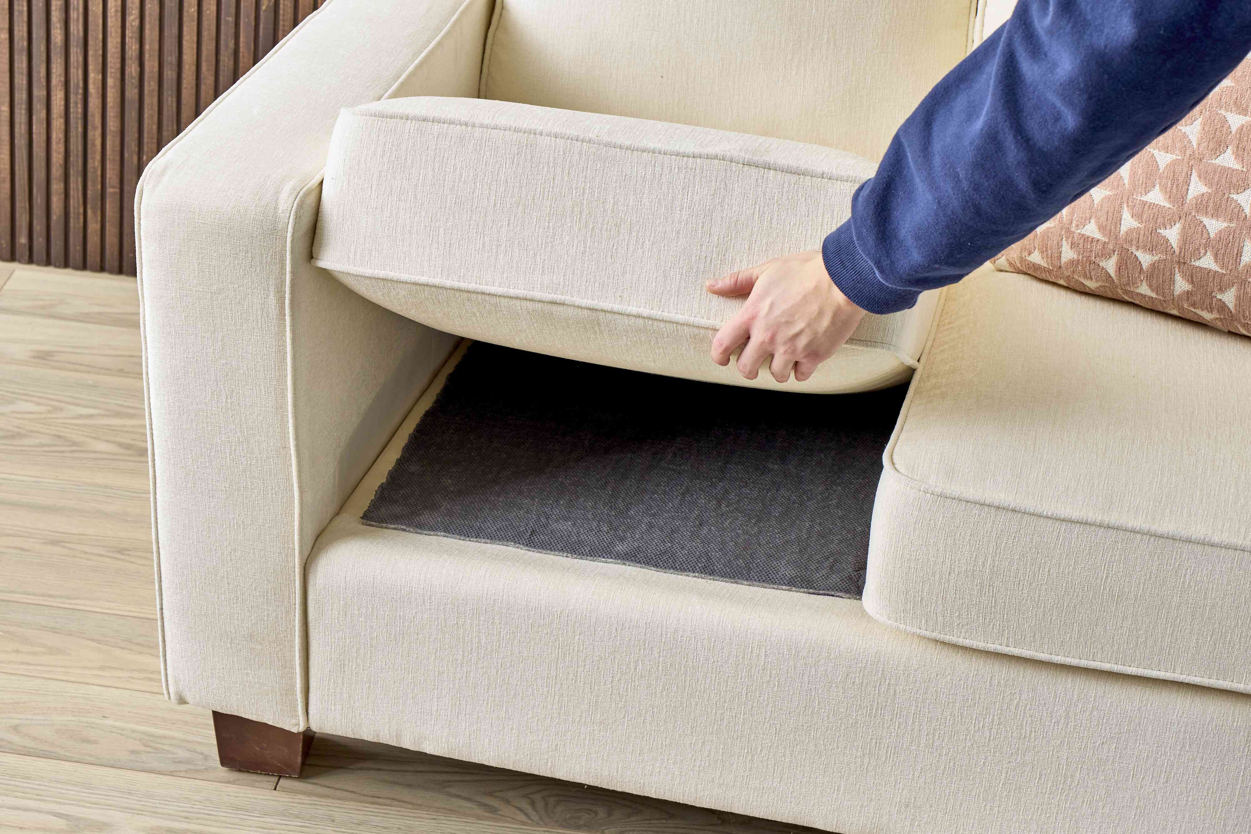A sofa seat cushion flipped upside down showing small removable hook and loop tabs placed near the back edge, realistic indoor photo
