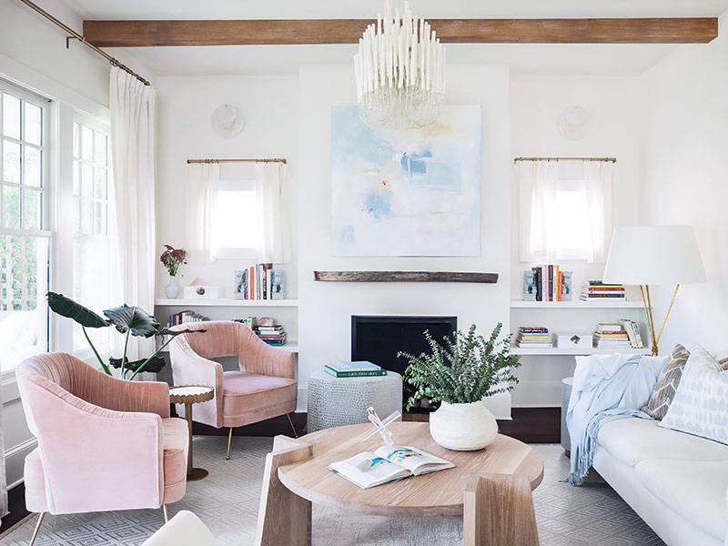 A styled living room coffee table with a brass tray, a tall ceramic vase with olive branches, two stacked art books, and a small stone bowl, evening lamp glow