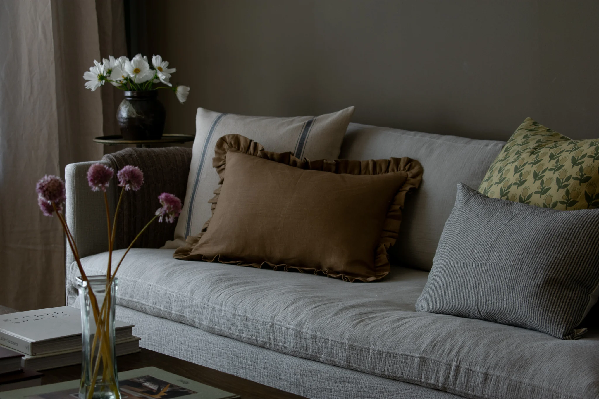 A washed linen throw pillow with a soft ruffled edge on a neutral sofa in warm afternoon light, real photo