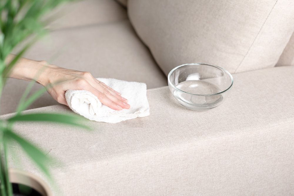 A white cotton cloth lightly dampened, blotting a small sticky spot on a blue upholstery cushion, close-up photo showing careful dabbing
