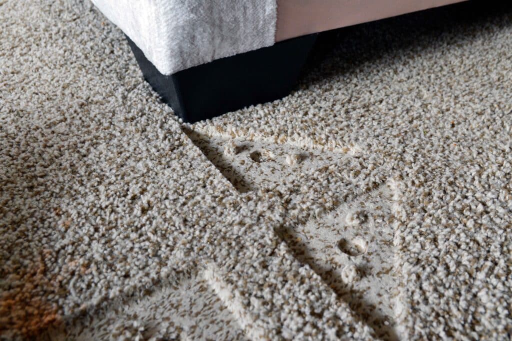 An area rug partially flipped back on a wood floor while someone massages the dented area from the underside