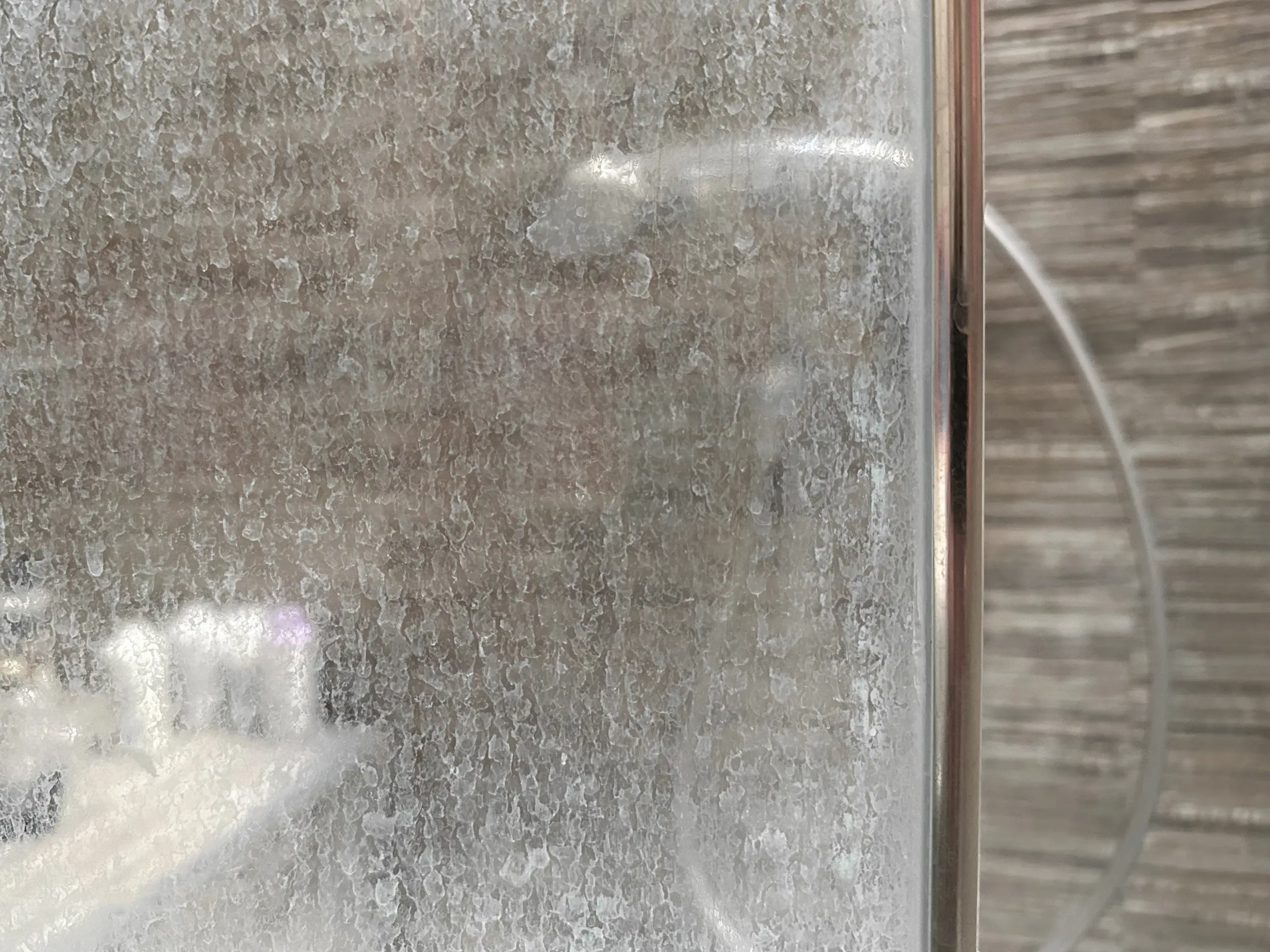 Close-up of a glass shower door with white mineral spots and streaks near the bottom edge, real photo