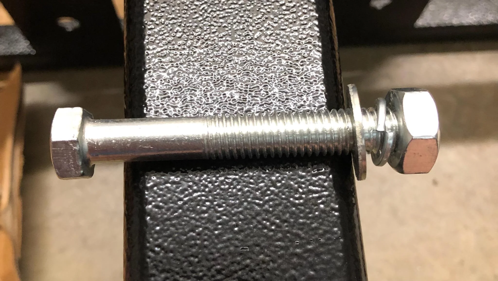 Close-up of a hand placing a small washer onto a bolt at a sofa metal corner bracket before tightening with a wrench