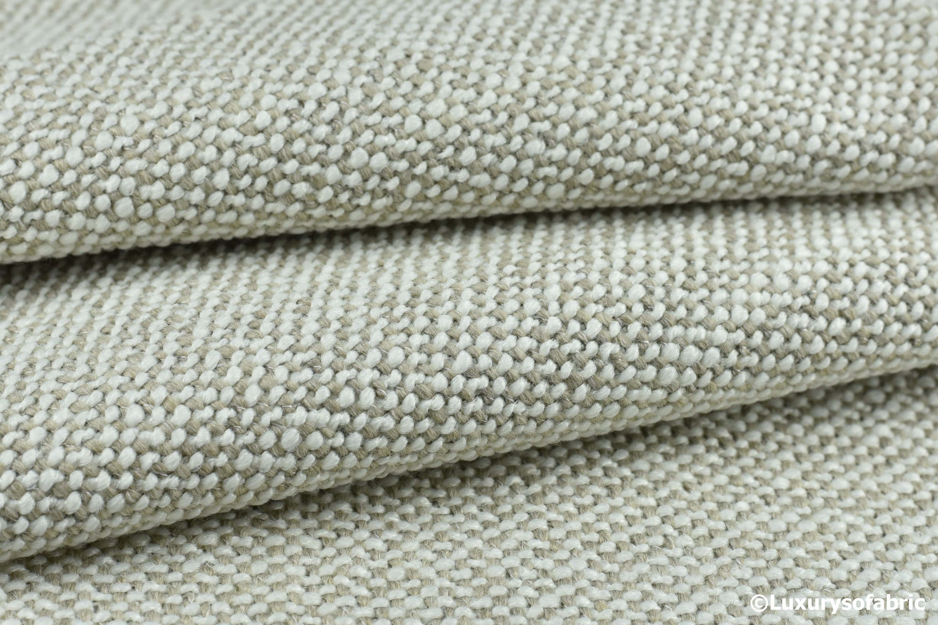 Close-up of a hand touching tightly woven gray upholstery fabric on a sofa cushion, showing texture and weave detail in natural window light