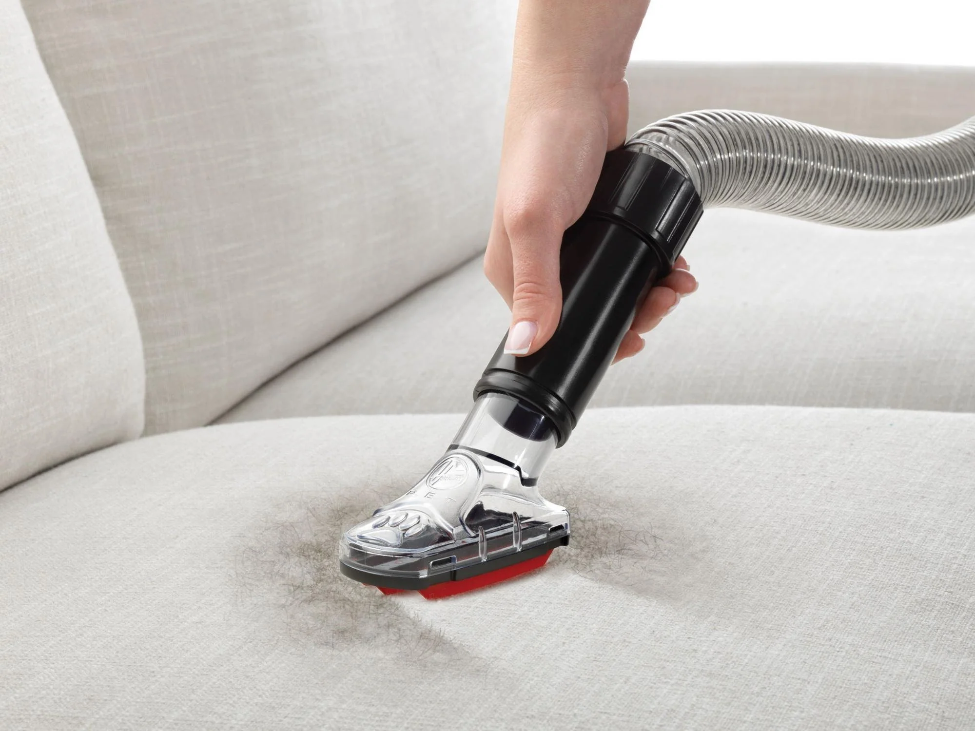 Close-up of a person vacuuming a couch seat cushion with an upholstery attachment in a softly lit living room, realistic photo