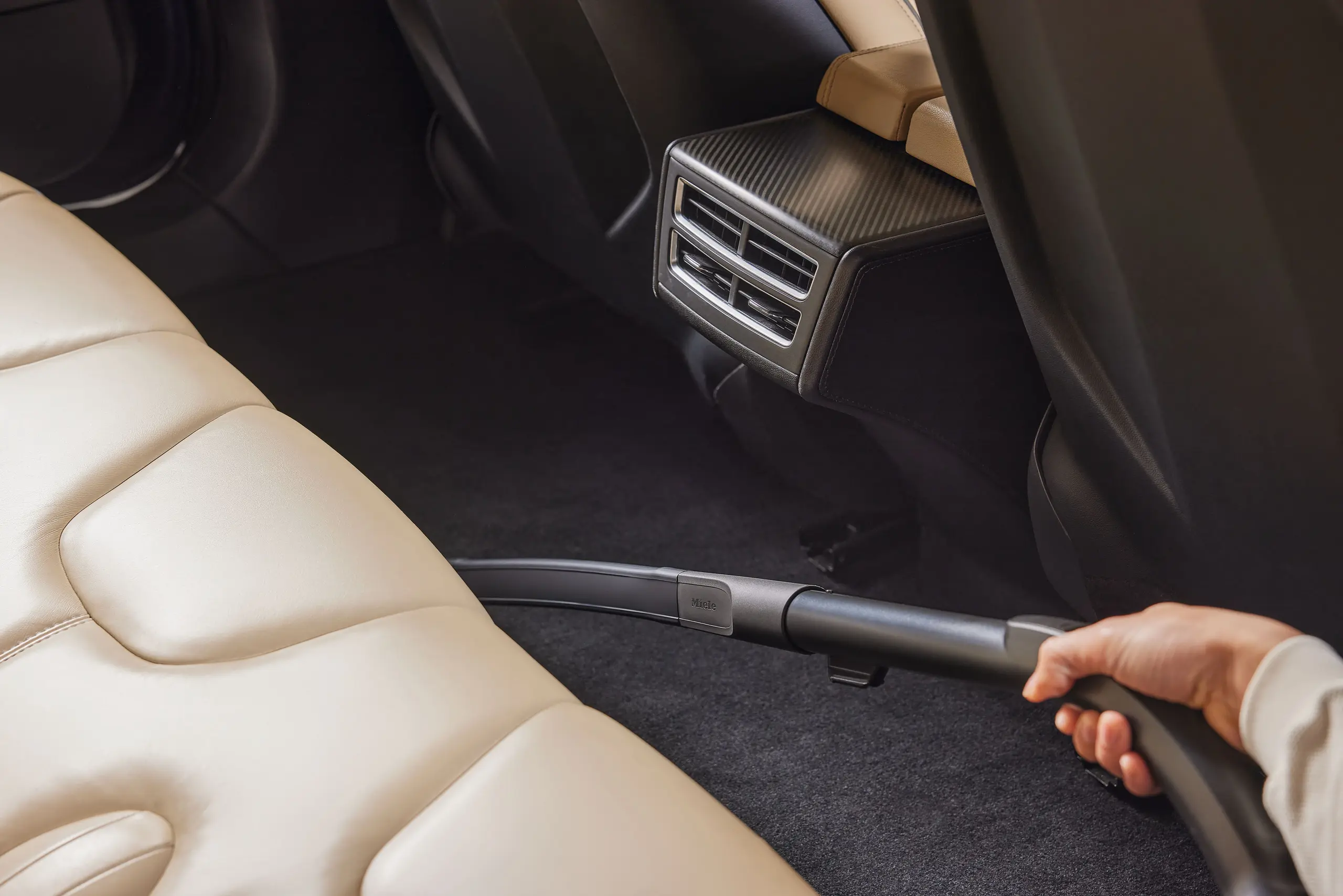Close-up of a vacuum crevice tool cleaning crumbs from the seam between a recliner seat and backrest, realistic indoor photo