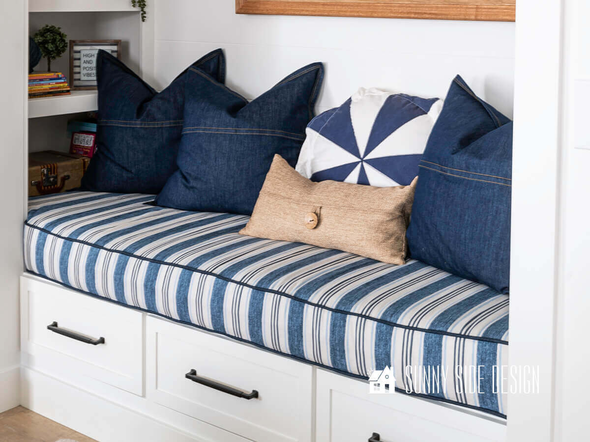 Close-up of the underside of an upholstered bench cushion showing a zipper opening and a fabric tag, photographed on a wooden floor